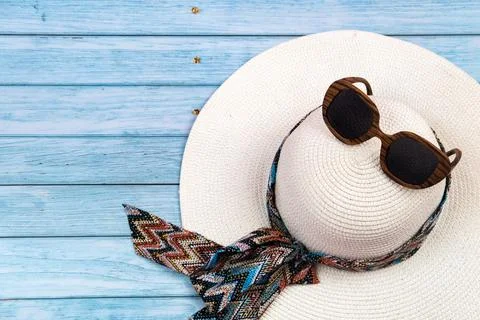Top view of a straw white hat with glasses lying on a blue wooden background. Stock Photos