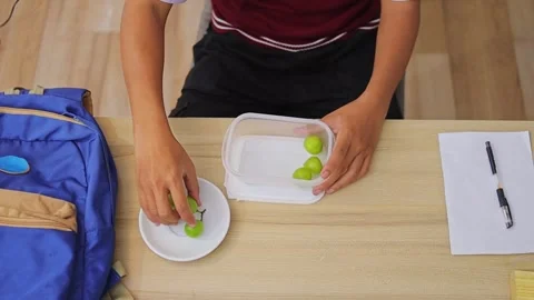Top view of student packing fresh green grapes into plastic lunch box on wooden Stock Footage 335017955