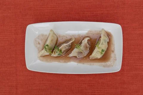 Top view of stuffed dumplings served in a rectangular white plate on a red table Stock Photos