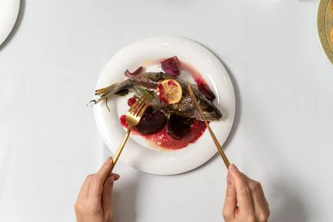 Top view stuffed fish on a white plate. Hands of a girl with gilded appliance Stock Photos