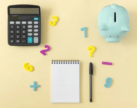 Top view of a table with a calculator, notepad, piggy bank and numbers. The Stock Photos