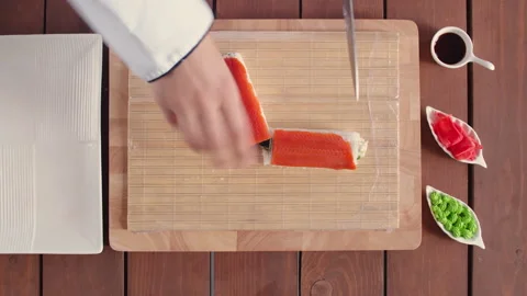 Top view of table with cutting board, mat and fish roll cut with knife, next to Stock Footage 145880084