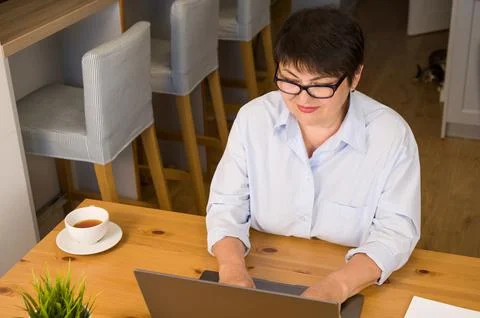Top view on table with laptop.cup of tes and notebook with senior woman worki Stock Photos