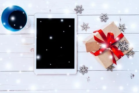 Top view tablet, coffee cup and gift box with snow and snowflakes on white .. Stock Photos