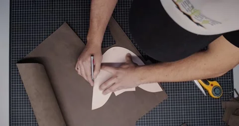 Top view of tailor with knife passing around pattern on leather piece preparing Video stock 200127092