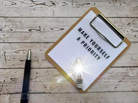 Top view of text on notepad - Make yourself a priority. With light bulb, pen and Stock Photos