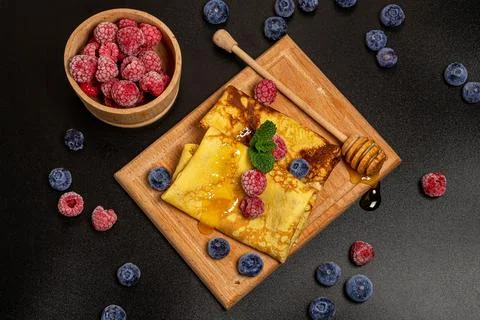 Top view, thin pancakes with berries, mint leaves and honey, dark background Stock Photos