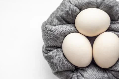 Top view of three beige eggs lying on a small gray pillow. Stock Photos