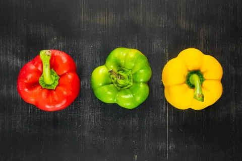 Top view of three fresh bright bell peppers on black rustic background Stock Photos