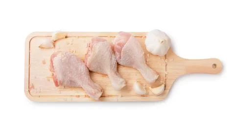 Top view of three raw chicken drumsticks on a wooden board with garlic and .. Stock Photos