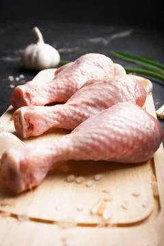 Top view of three raw chicken drumsticks on a wooden cutting board with gar.. Stock Photos