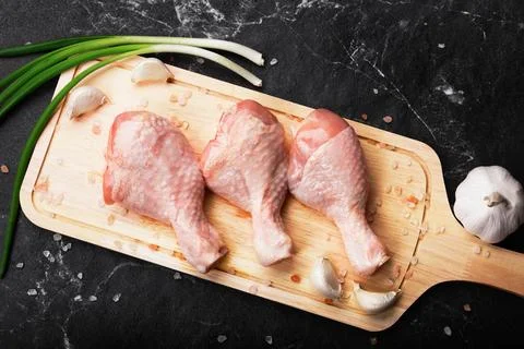 Top view of three raw chicken drumsticks on a wooden cutting board with gar.. Stock Photos