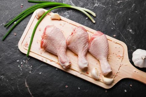 Top view of three raw chicken drumsticks on a wooden cutting board with gre.. Foto stock