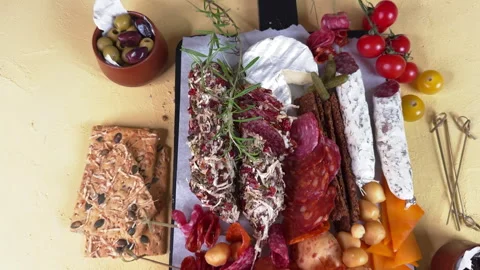 Top view through greenery of a wooden board with meat and cheese appetizers on a Видео 304459123