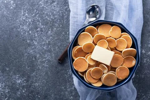 Top view tiny cereal pancakes with butter in blue bowl, spoon on blue gauze o Stock Photos