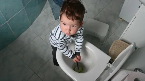Top view of toddler boy in striped clothes washes a toilet with a cleaning brush Stock Footage 171381483