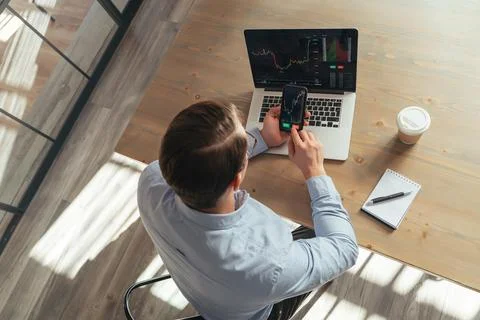 Top view of trader at office table holding phone with opened money investment Stock Photos