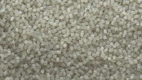 Top view of translucent plastic pellets rotating slowly, creating industrial Stock Footage 334657632
