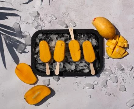 Top view of tray of mango popsicles on white background in sun. Stock Photos
