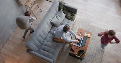 Top view two children run around stressed young mother trying to work from home Stock Footage 129134177