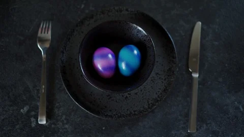 Top view of two colorful Easter eggs on a black plate. Woman's hand takes blue 库存影片 116417914