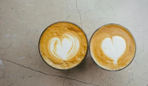 Top view of two glasses of coffee with art hearts on foam on marble background. Stock Photos