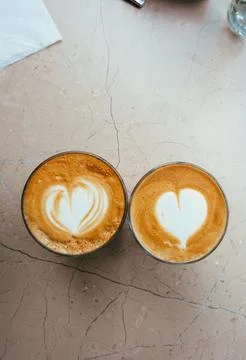 Top view of two glasses of coffee with art hearts on foam on marble background. Stock Photos