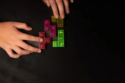 Top view of two hands assembling colorful transparent puzzle blocks on a blac Stock Photos
