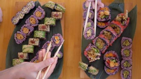 Top view of two hands picking up sushi rolls from wooden trays full of sushi 스톡 사진
