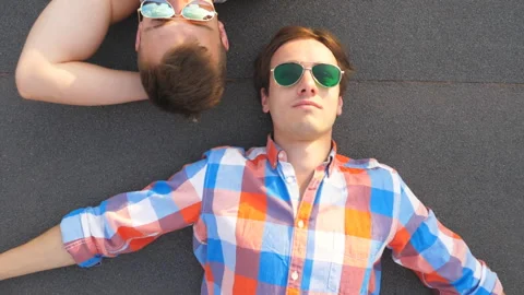 Top view of two handsome guys in sunglasses lying together at the roof of house Stock Footage 310233360