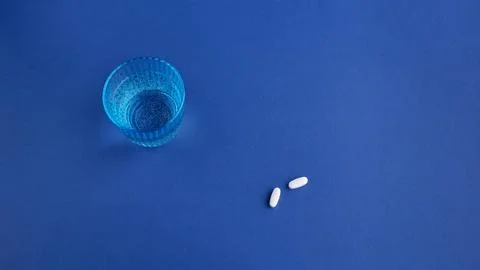 Top view of two white round medical pills, vitamins, a beautiful blue glass w Stock Photos