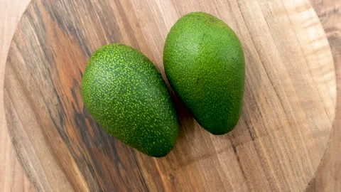 Top view of Two Whole Avocado fruits rotating on a wooden surface Stock Footage 272220269
