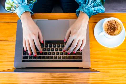 Top view of two woman's hands working on a laptop while drinking a cappuccino Stock Photos
