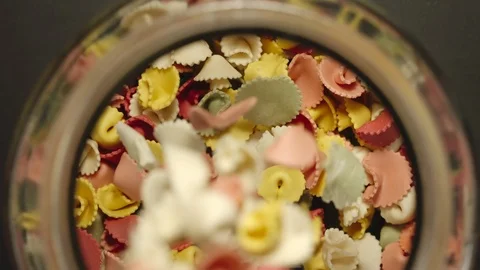 TOP VIEW: Uncooked colour figural pasta fall into glass jar - Slow Motion Stock Footage 103362409