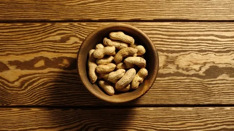 TOP VIEW: Unpeeled peanuts appear in wooden cup and full this cup - Stop motion Stock Footage 96799761
