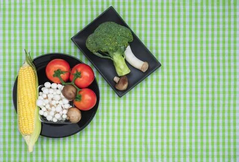 Top view of various fresh vegetables in black plates on green plaid tableclot Stock Photos