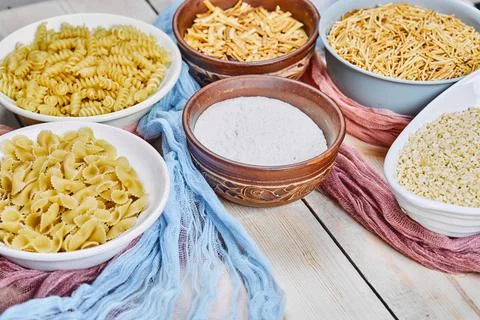 Top view of various raw pastas and bowl of flour on wooden table Stock Photos