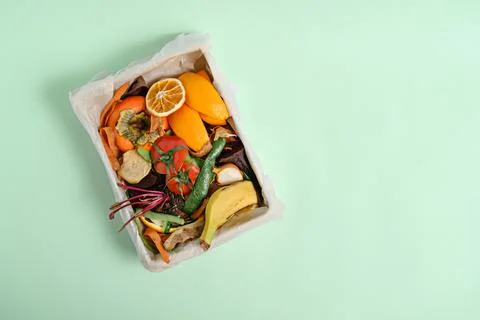 Top view vegetable peels in compost bin on green background, compost concept. Stock Photos