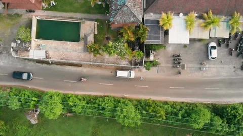 Top view of vehicles driving on road next to house with motorbikes parked, Bali Stock Footage 140282242