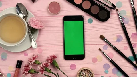 Top view of vertical mobile phone with green screen on pink wooden table with Stock Footage 73910820