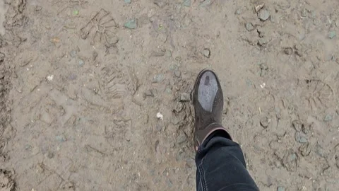 Top view of walking feet in brown rain rubber boots and black jeans on offroad d Stock Footage 335589975