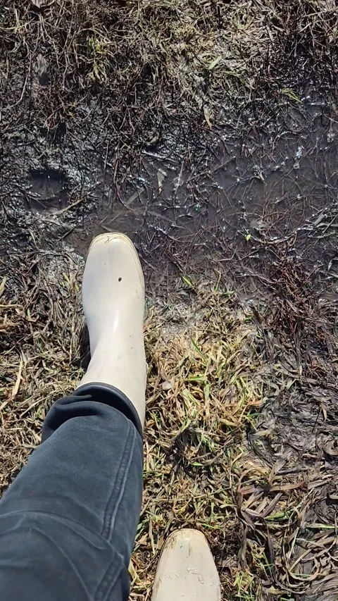 Top view of walking feet in white rain rubber boots and black jeans on offroad Stock Footage 332211880