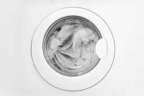 Top view of a washing machine drum filled with soapy water and white laundr.. Stock Photos