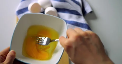Top view of whisking eggs in white bowl with fork, hand holding utensil over Stock Footage 315692557