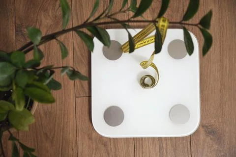 Top view of white bathroom scale with yellow measuring tape on wooden floor.. Stock Photos