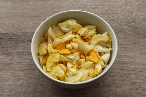Top view of a white ceramic bowl filled with sliced boiled eggs and potatoes. Stock-Fotos