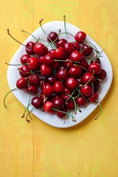 Top view of a white ceramic plate filled with ripe red cherries on a bright y 库存照片