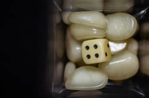Top view of a white dice and white plastic stones in a glass bottle with black b Stock Photos