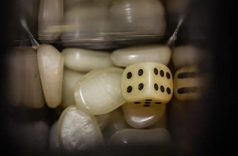 Top view of a white dice and white plastic stones in a glass bottle with black b Stock Photos