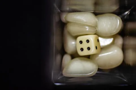 Top view of a white dice and white plastic stones in a glass bottle with black b Stock Photos